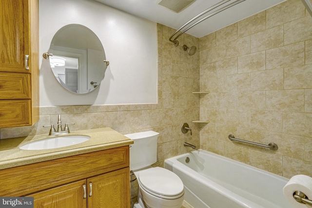 full bathroom featuring tiled shower / bath, vanity, toilet, and tile walls