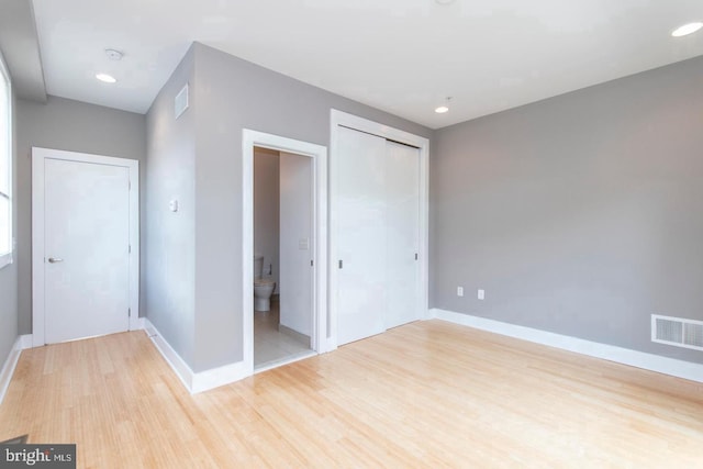 unfurnished bedroom with light wood-type flooring, connected bathroom, and a closet