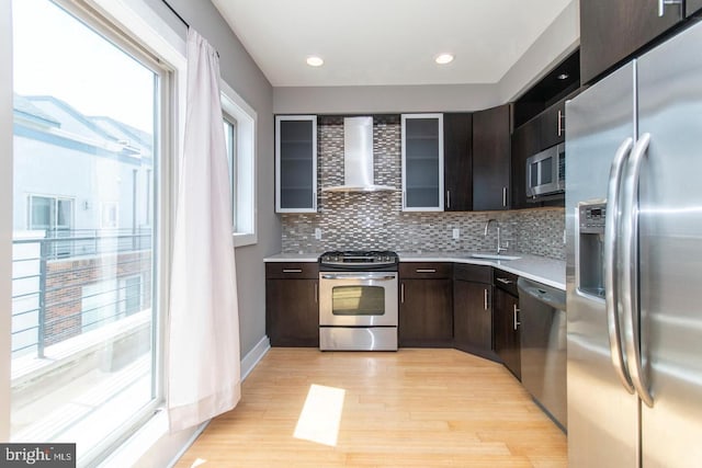 kitchen with dark brown cabinetry, sink, wall chimney exhaust hood, stainless steel appliances, and light wood-type flooring