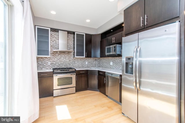 kitchen with dark brown cabinets, light hardwood / wood-style flooring, stainless steel appliances, and wall chimney range hood