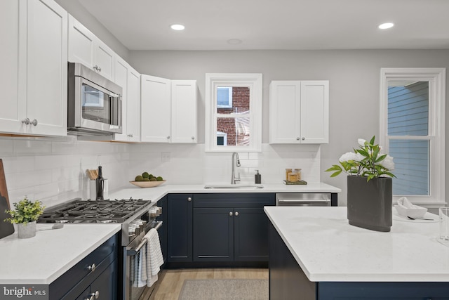 kitchen featuring decorative backsplash, stainless steel appliances, sink, white cabinets, and light hardwood / wood-style floors