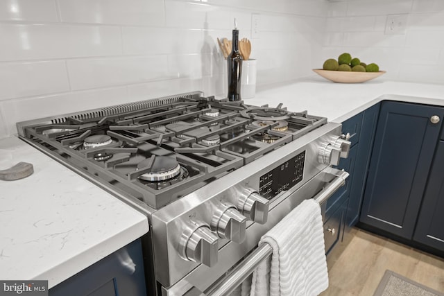 details featuring backsplash, stainless steel stove, and light hardwood / wood-style flooring