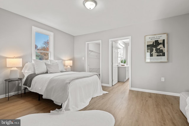 bedroom with ensuite bathroom, a closet, a walk in closet, and light hardwood / wood-style flooring