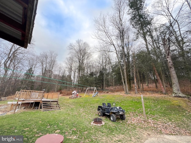 view of yard featuring a playground, a deck, and an outdoor fire pit