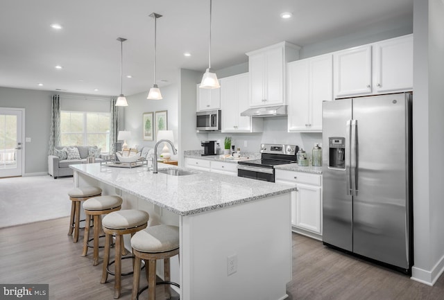 kitchen with white cabinets, a center island with sink, stainless steel appliances, and hanging light fixtures