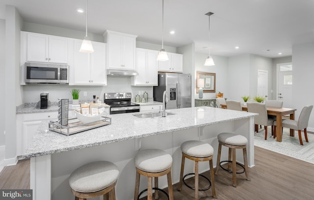 kitchen with a kitchen island with sink, hanging light fixtures, dark wood-type flooring, and appliances with stainless steel finishes