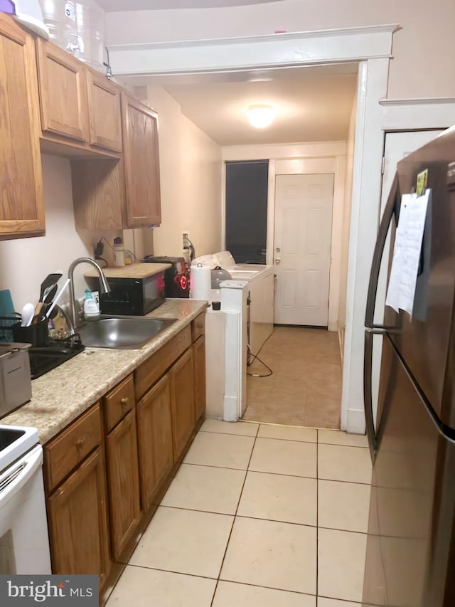 kitchen with independent washer and dryer, light tile patterned floors, stainless steel refrigerator, white electric range, and sink