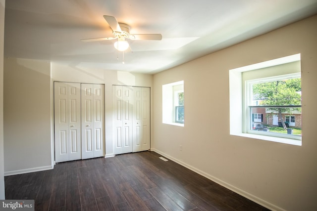 unfurnished bedroom featuring ceiling fan, dark hardwood / wood-style flooring, and two closets