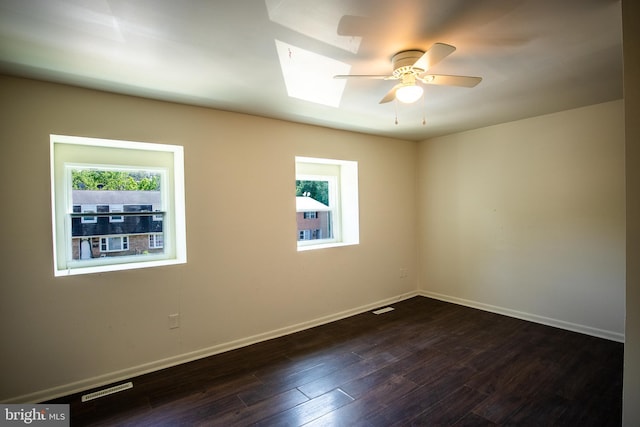 unfurnished room with ceiling fan, a healthy amount of sunlight, dark hardwood / wood-style flooring, and a skylight