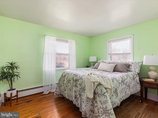 bedroom with hardwood / wood-style floors, multiple windows, and a baseboard heating unit