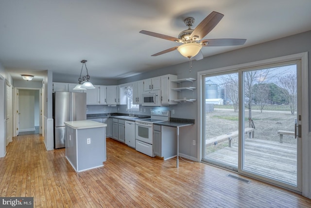 kitchen with sink, light hardwood / wood-style flooring, decorative light fixtures, white appliances, and a kitchen island