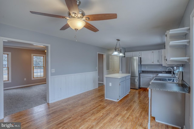 kitchen featuring a kitchen island, sink, white cabinetry, hanging light fixtures, and stainless steel refrigerator