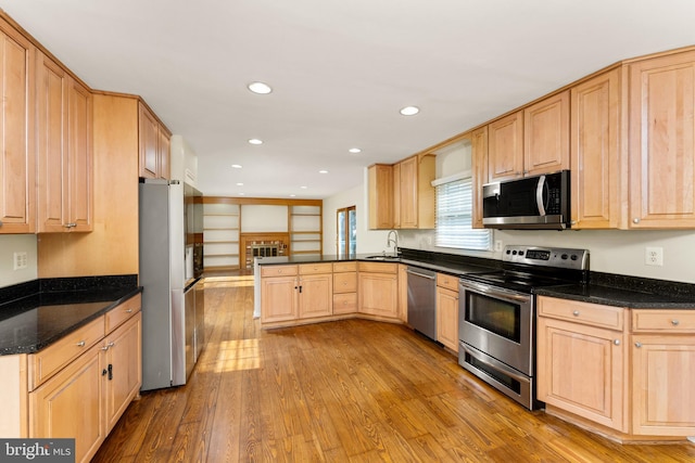 kitchen with dark stone counters, stainless steel appliances, sink, light brown cabinets, and light hardwood / wood-style flooring