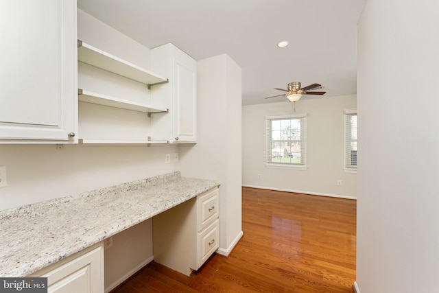 kitchen with light stone countertops, ceiling fan, hardwood / wood-style floors, white cabinets, and built in desk