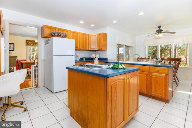 kitchen with ceiling fan, white fridge, a kitchen island, and sink