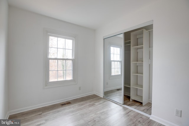 unfurnished bedroom with a closet, light hardwood / wood-style flooring, and multiple windows