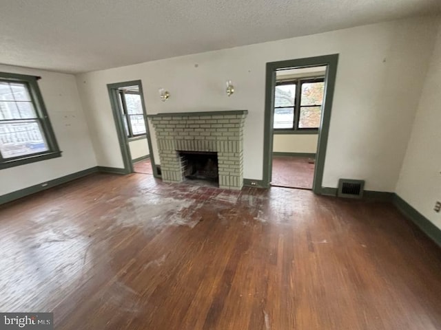 unfurnished living room with dark wood-type flooring, a textured ceiling, and a brick fireplace