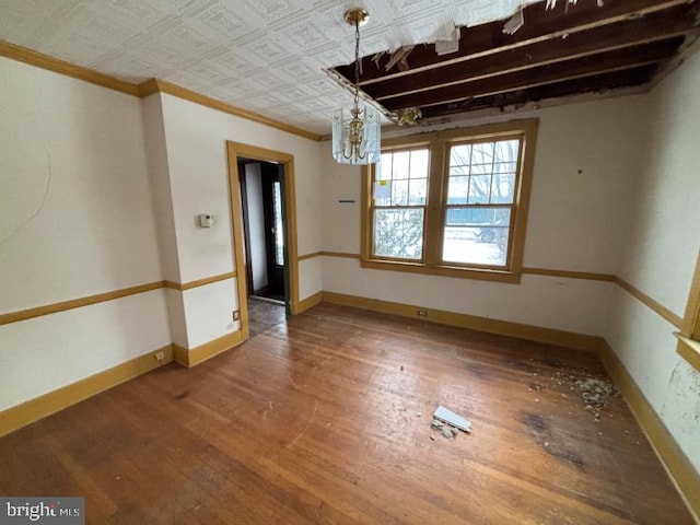 empty room featuring hardwood / wood-style floors, ornamental molding, and a notable chandelier