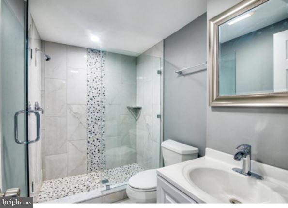 bathroom featuring vanity, a shower with shower door, and toilet