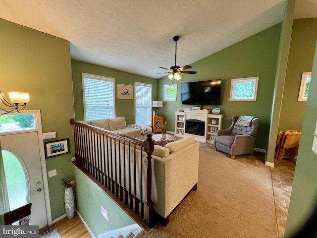 carpeted living room featuring a textured ceiling, ceiling fan with notable chandelier, and vaulted ceiling