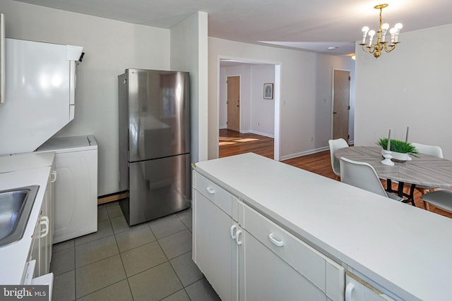 kitchen with hanging light fixtures, white cabinetry, sink, and stainless steel refrigerator