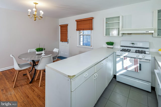 kitchen with white gas range, decorative light fixtures, white cabinets, and kitchen peninsula