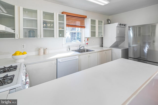 kitchen featuring white appliances, stacked washing maching and dryer, sink, and white cabinets