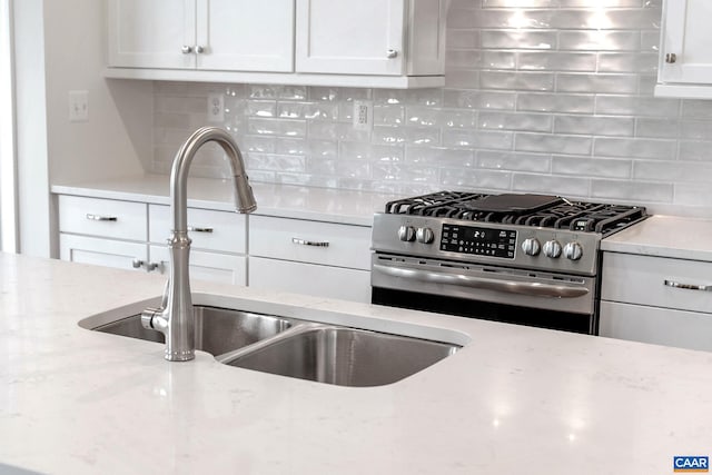 kitchen featuring tasteful backsplash, stainless steel gas range oven, light stone countertops, and sink