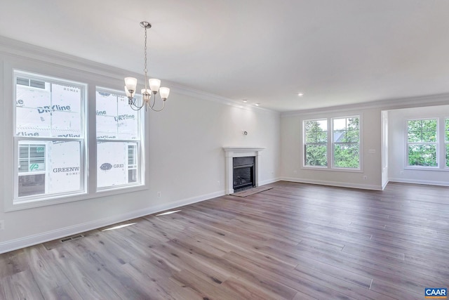 unfurnished living room featuring crown molding, a chandelier, hardwood / wood-style floors, and a healthy amount of sunlight