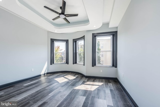 empty room featuring ceiling fan, dark wood-type flooring, and a tray ceiling