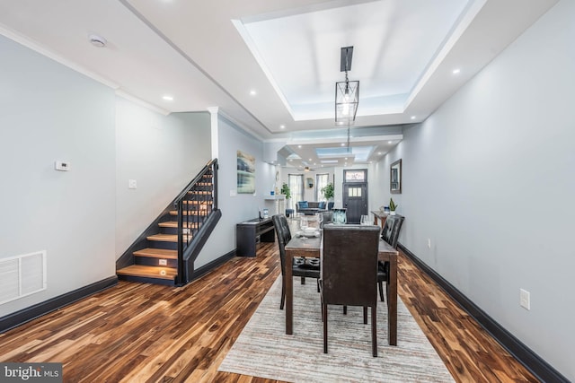 dining area with a tray ceiling, crown molding, and wood-type flooring