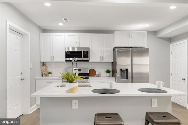 kitchen with decorative backsplash, appliances with stainless steel finishes, a kitchen breakfast bar, a center island with sink, and white cabinetry