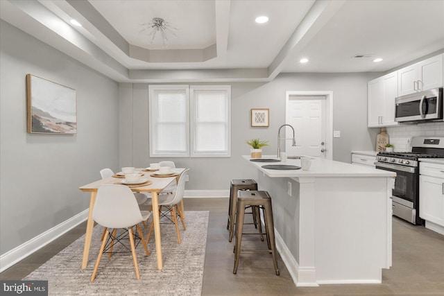 kitchen with white cabinetry, a kitchen breakfast bar, backsplash, a center island with sink, and appliances with stainless steel finishes