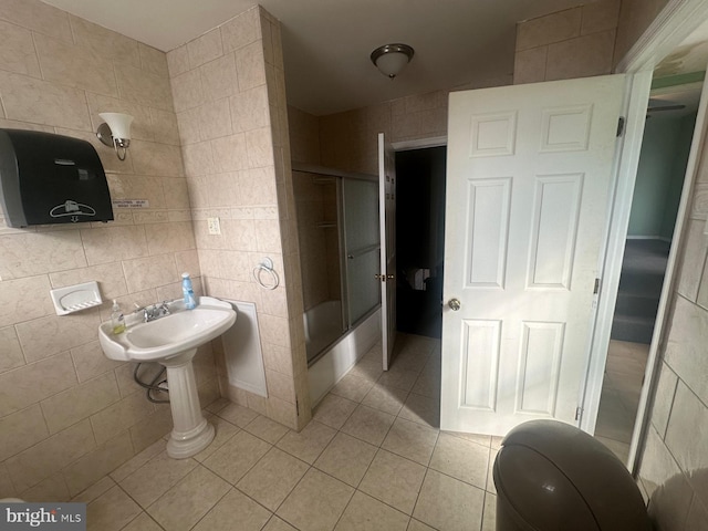 bathroom featuring tile patterned flooring, enclosed tub / shower combo, tile walls, and sink