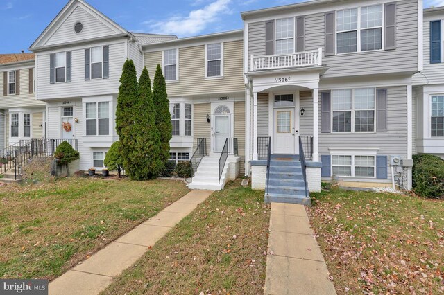 view of property featuring a balcony and a front lawn