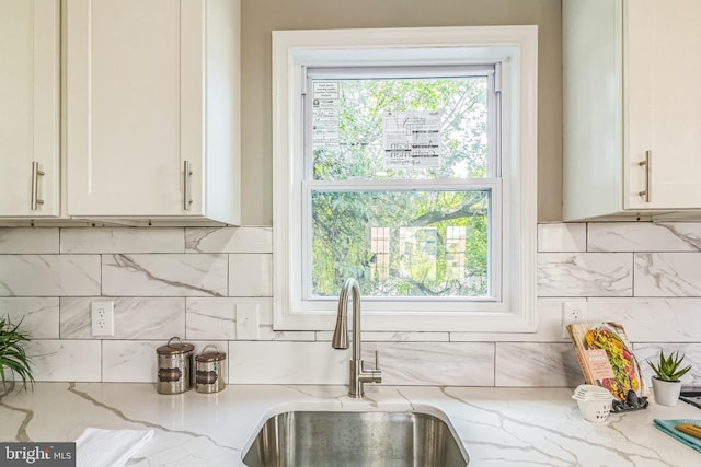 interior details featuring white cabinets, backsplash, light stone counters, and sink