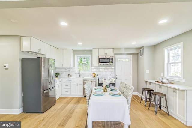 kitchen with white cabinets, a breakfast bar, stainless steel appliances, and light hardwood / wood-style flooring