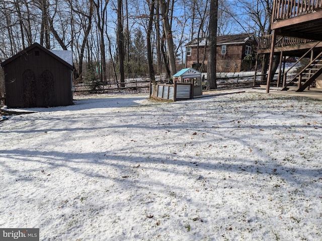 yard covered in snow with a deck, an outdoor structure, stairway, and a shed