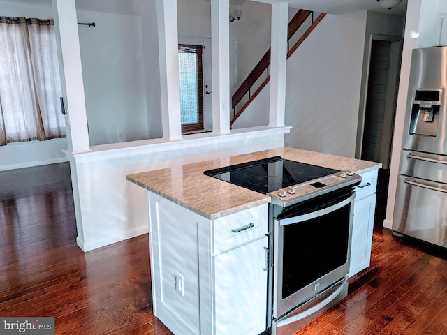 kitchen with light stone countertops, a kitchen island, dark wood-style flooring, appliances with stainless steel finishes, and white cabinetry