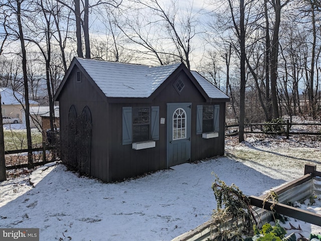 snow covered structure featuring an outbuilding and fence