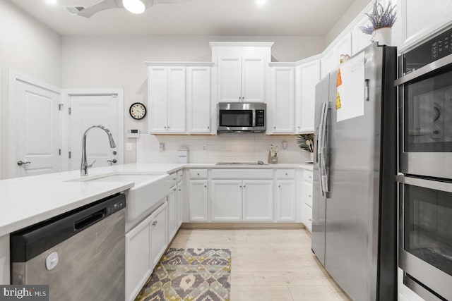 kitchen with backsplash, white cabinets, sink, light wood-type flooring, and stainless steel appliances