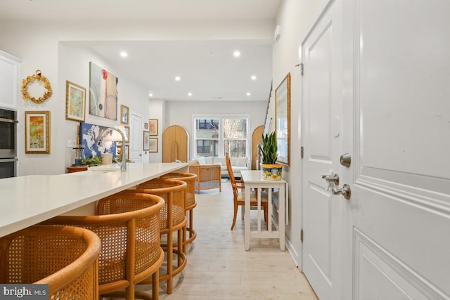 kitchen with light hardwood / wood-style floors, a kitchen bar, sink, and double oven