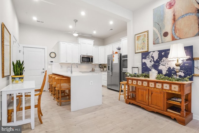 kitchen featuring stainless steel appliances, a kitchen breakfast bar, kitchen peninsula, white cabinets, and light wood-type flooring