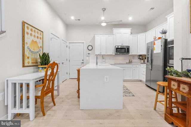 kitchen with white cabinetry, ceiling fan, decorative backsplash, appliances with stainless steel finishes, and light wood-type flooring