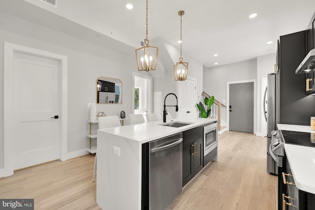 kitchen featuring sink, hanging light fixtures, stainless steel appliances, a kitchen island with sink, and light wood-type flooring