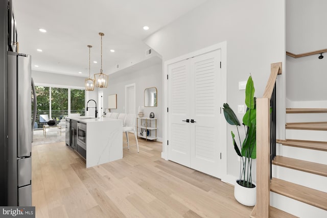 kitchen featuring stainless steel refrigerator, sink, an island with sink, pendant lighting, and light hardwood / wood-style floors