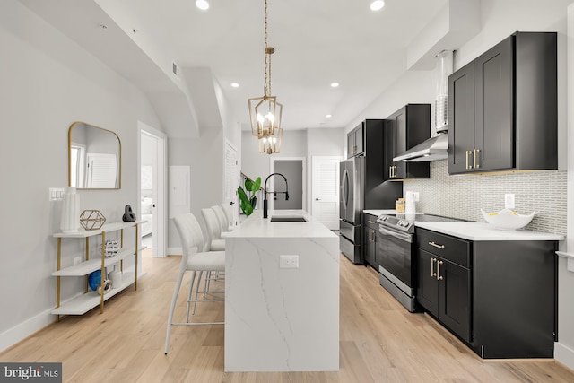 kitchen with sink, stainless steel appliances, an island with sink, pendant lighting, and light hardwood / wood-style floors