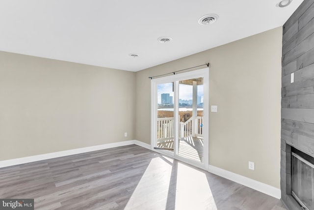 unfurnished living room with a tiled fireplace and light wood-type flooring