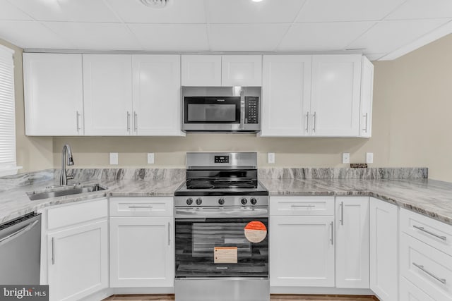 kitchen featuring light stone countertops, stainless steel appliances, white cabinetry, and sink