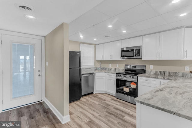 kitchen with white cabinets, light stone counters, stainless steel appliances, and light hardwood / wood-style flooring